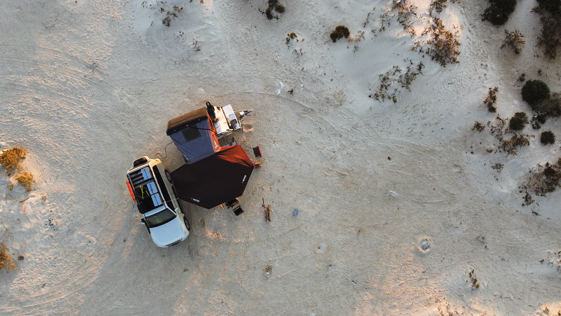 Luftaufnahme eines Kuckoo Campers mit Dachzelt neben einem Geländefahrzeug in der Wüste